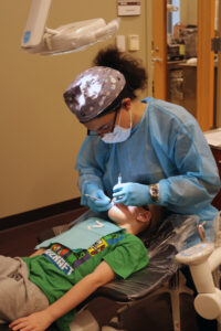 Dental hygiene student examines a boy's mouth in clinic.